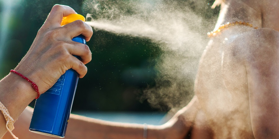 Unrecognizable mother spraying suntan lotion on her son's body at the beach.