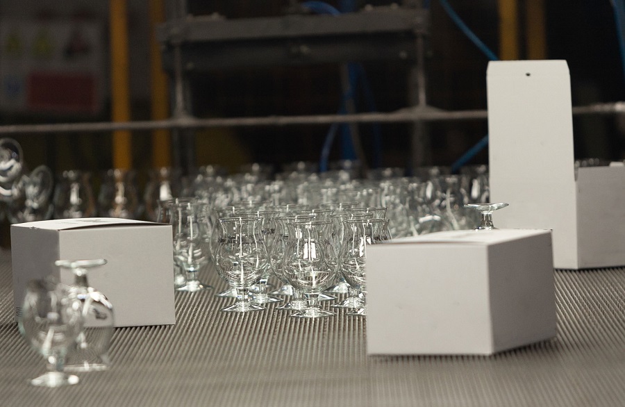 Close-up view of the hands of a manufacturing worker putting drink glasses in cardboard boxes before delivery to customer in a glassware factory. Selling and shipping export concept.